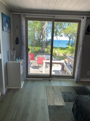 A room with a sliding glass door leading to an outdoor patio with a table and chairs, a small refrigerator, and a painting on the wall.