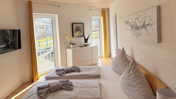 A bedroom with a wooden bed, two pillows, a bedside table with a lamp, a dresser, and a painting on the wall. - Auszeit in Willingen - Erdgeschoss Wohnung (Willingen)