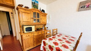 Quarto com armários de madeira, micro-ondas, mesa com toalha de mesa florida vermelha e porta que dá para outro espaço.