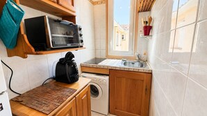 Uma cozinha compacta com forno embutido, máquina de lavar e janela.