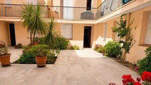 Um pátio com vasos de plantas, piso de azulejos e uma varanda com guarda-corpo.