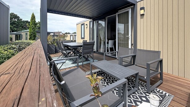A covered outdoor seating area with a table and chairs, a wooden deck, and a patterned rug. - Mobil-home in the heart of Jullouville - 6 guests (Jullouville)