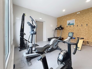 Ein Fitnessraum mit Cardiogeräten, einem Rudergerät und einem an der Wand befestigten Fernseher.