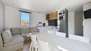 A modern kitchen with white cabinetry, a stainless steel refrigerator, and a dining area with a white table and chairs. - Mobil-home in the heart of Jullouville - 6 guests (Jullouville)