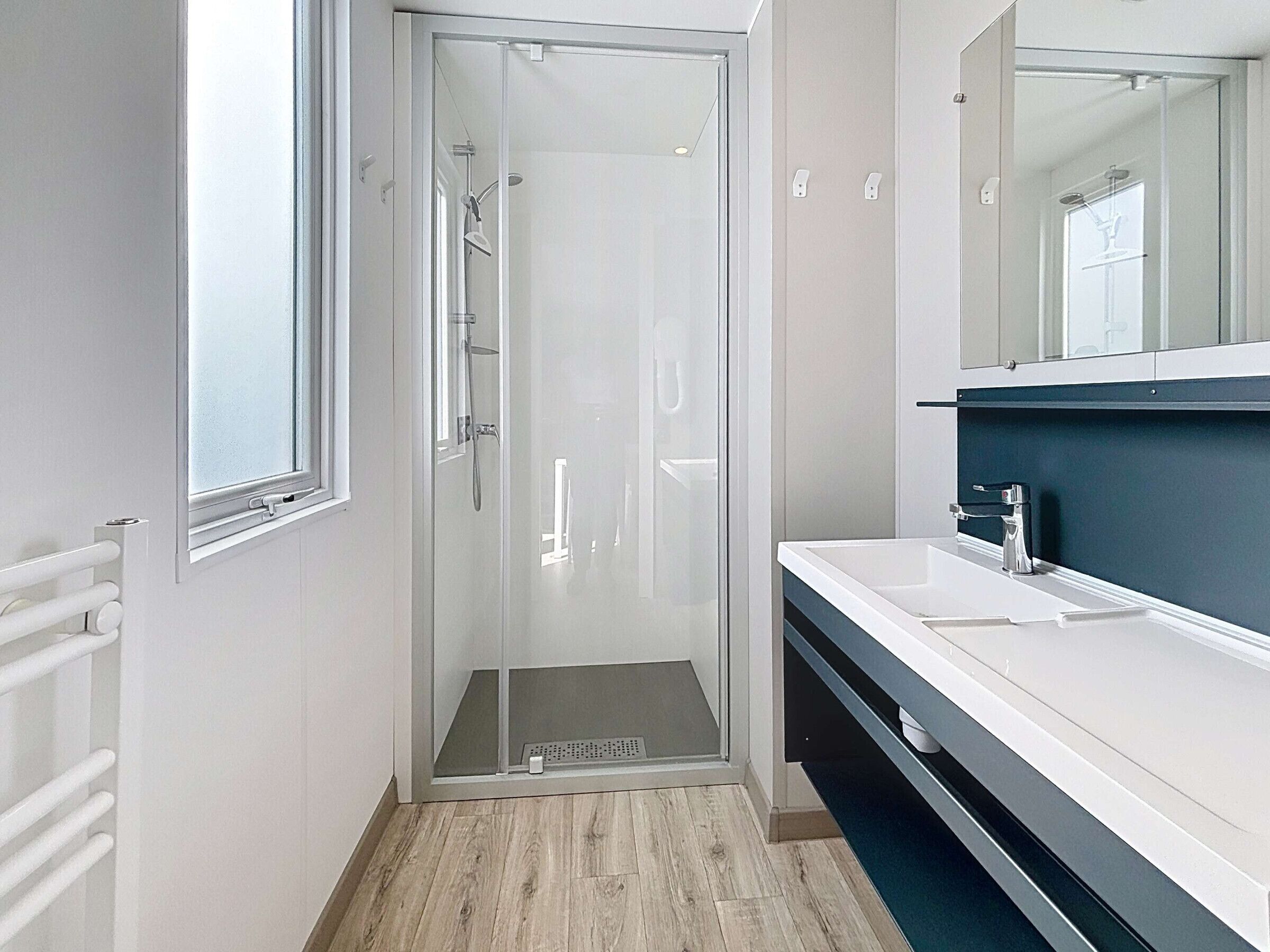 Une salle de bain moderne avec une douche à parois de verre, un lavabo blanc et un meuble-lavabo de couleur foncée.