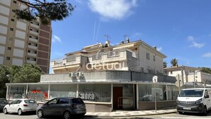 Un bâtiment avec une façade vitrée, une entrée bien visible et des voitures garées devant.