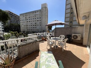 Eine Dachterrasse mit Tisch und Stühlen, einem Blumentopf und Blick auf umliegende Gebäude.