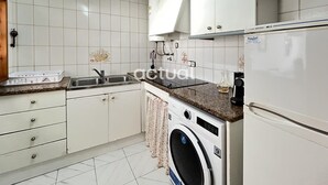 Une cuisine avec des meubles blancs, un évier, une cuisinière, un lave-linge et un réfrigérateur.