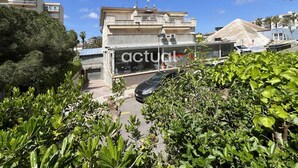 Un bâtiment doté d’un balcon, une voiture garée devant et de la verdure au premier plan.