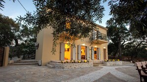 A two-story building with a stone patio, a balcony, and a tree in the foreground. - Villa Praxithea (Lakka)