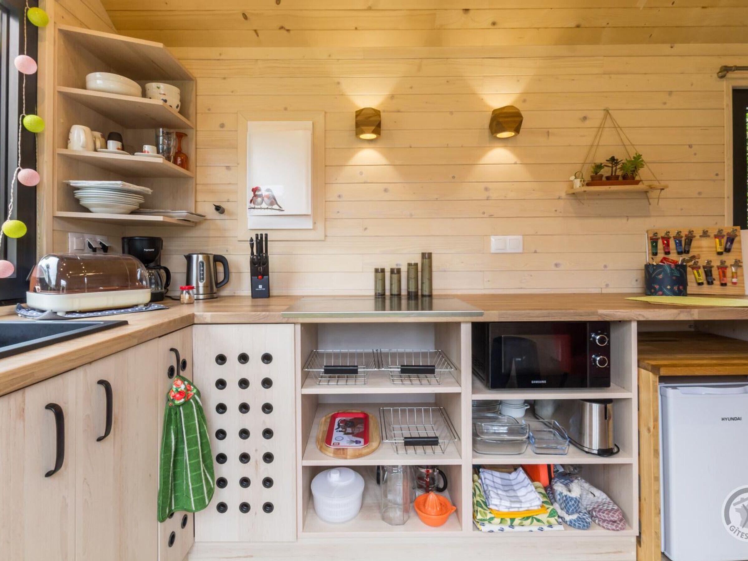 Une cuisine compacte dotée de meubles en bois, d’un four à micro-ondes, d’un réfrigérateur Samsung et d’un porte-casseroles suspendu.
