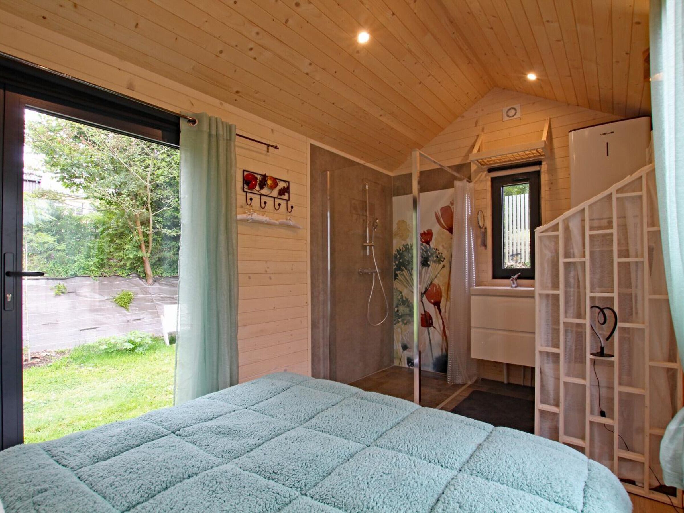 A bedroom with a bed, a shower, a window, and a door leading to a bathroom.