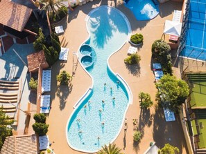 An aerial view of a swimming pool with a unique shape, surrounded by lounge chairs and palm trees. - Mobile home with AC - 6 guests (Canet-en-Roussillon)
