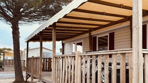 A wooden deck with a railing, a staircase leading to a covered porch, and a tree in the background. - Mobile home with AC - 6 guests (Canet-en-Roussillon)
