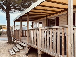 A wooden deck with a railing, a staircase leading to a covered porch, and a tree in the background. - Mobile home with AC - 6 guests (Canet-en-Roussillon)