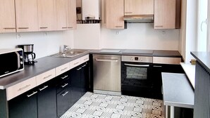 Une cuisine moderne avec des meubles de couleur bois clair, un lave-vaisselle en acier inoxydable, un four encastré et un plan de travail noir.