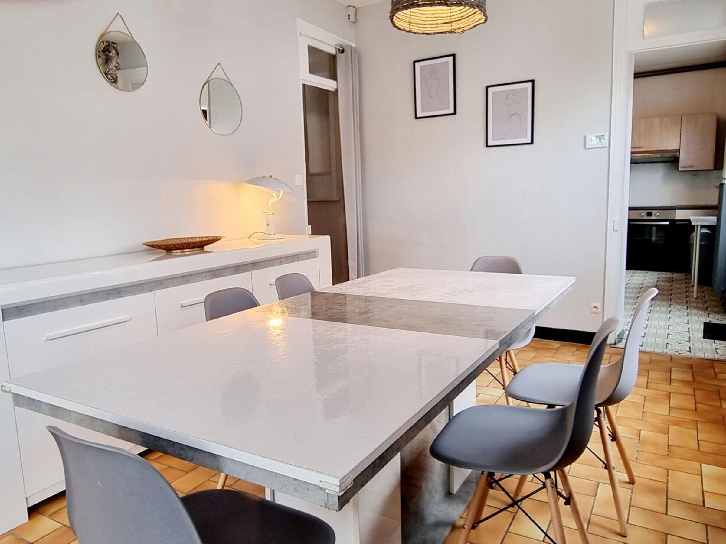 Une cuisine moderne avec un plan de travail blanc, une table à manger avec des chaises et un luminaire suspendu.