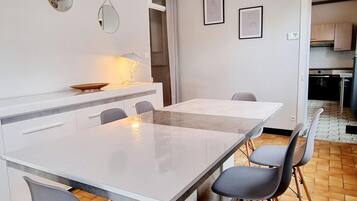 Une cuisine moderne avec un plan de travail blanc, une table à manger avec des chaises et un luminaire suspendu.