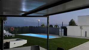 Ein überdachter Außenbereich mit Pool, Sitzgelegenheiten und Blick auf den Himmel.