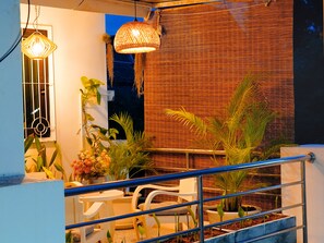 A balcony with a metal railing, potted plants, a white table, and two hanging light fixtures. - Old Town Hideaway/Walk Everwhere/Tha Phae Gate (Chang Wat Chiang Mai)