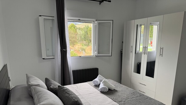 Ein Schlafzimmer mit Bett, Kissen, Heizkörper, Fenster und Kleiderschrank.