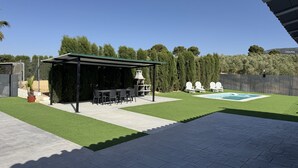 Eine Terrassenfläche mit überdachter Sitzgelegenheit, Grill und Pool.