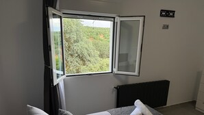 Une pièce avec un lit, une fenêtre dont le store est ouvert, un radiateur et un thermostat fixé au mur.