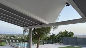 Un espace extérieur abrité, doté d’une piscine, d’un arbre et offrant une vue sur des collines lointaines.