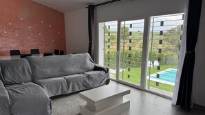 Un salon moderne avec un canapé gris, une table basse blanche et une grande porte-fenêtre coulissante donnant sur une piscine.