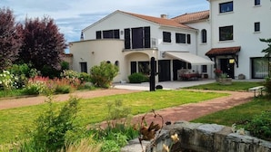 Una casa de dos pisos con un porche cubierto y un jardín con un estanque.