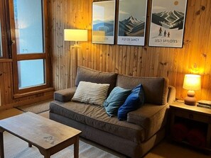 Une pièce chaleureuse avec un mur en bois, un canapé avec des coussins, une petite table et des tableaux encadrés.