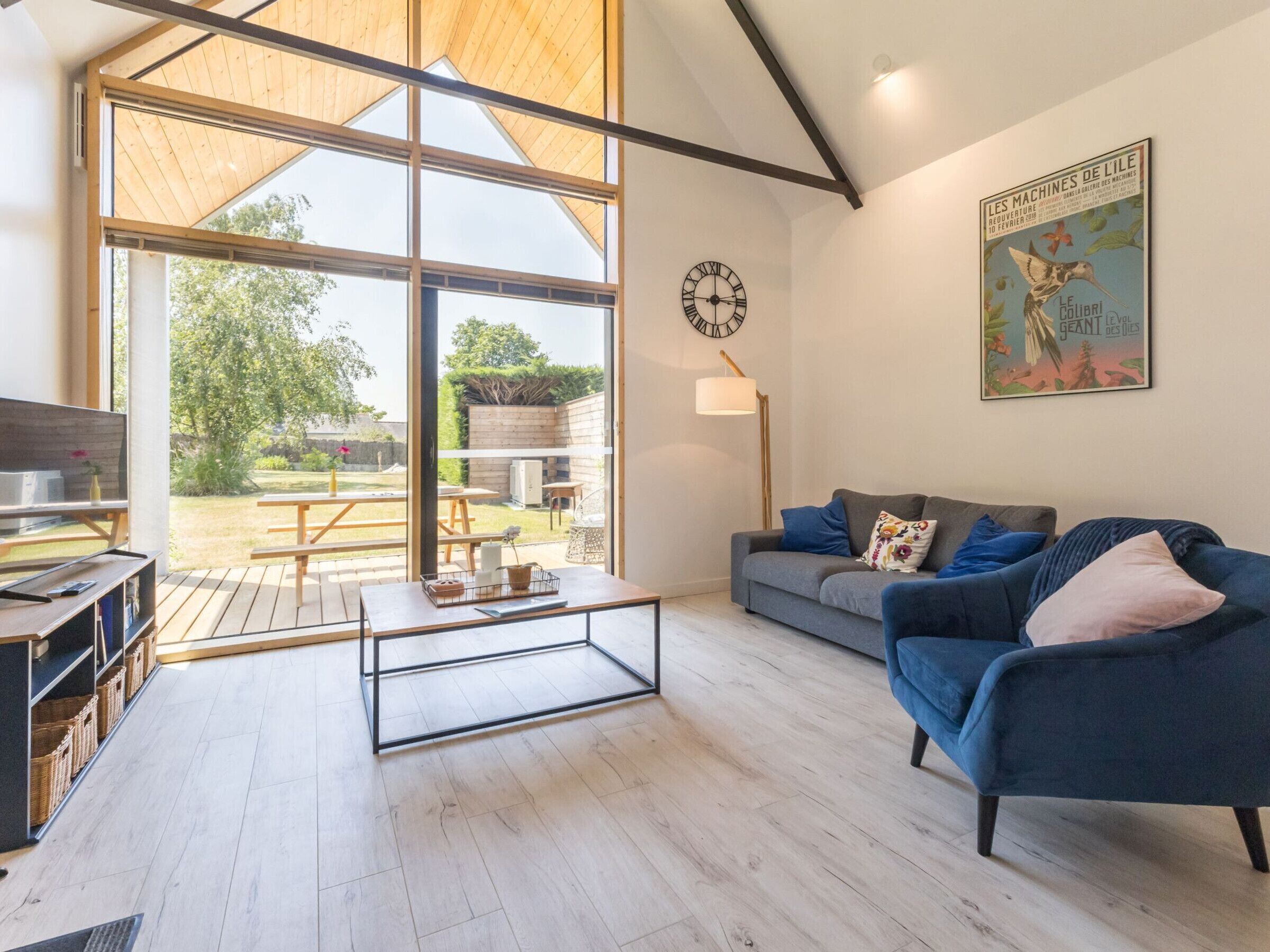 Un salon moderne avec une grande fenêtre, un canapé, une table basse et une horloge au mur.