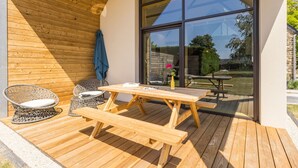 A wooden deck with a table and chairs, a large window, and a blue towel on the wall. - Cozy gîte near Nantes - max guests (Petit-Mars)