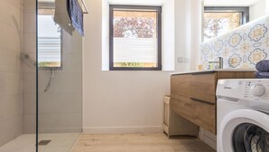 A compact laundry room with a washing machine, a glass shower enclosure, and a window providing natural light. - Cozy gîte near Nantes - max guests (Petit-Mars)