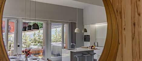 A modern kitchen with a dining area, large windows, and a view of the outdoors.