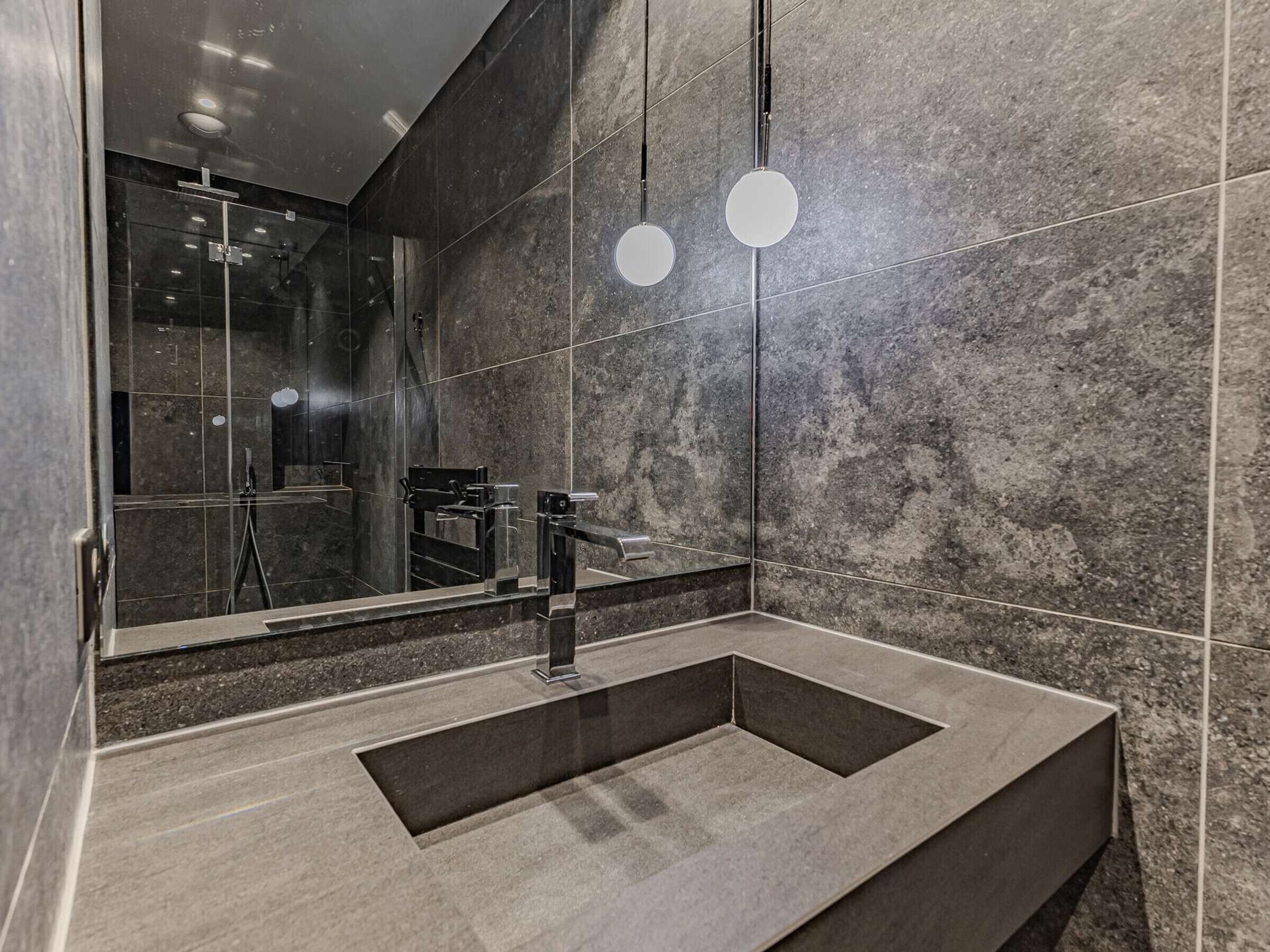 A modern bathroom with a rectangular sink, a large mirror, and two pendant lights.