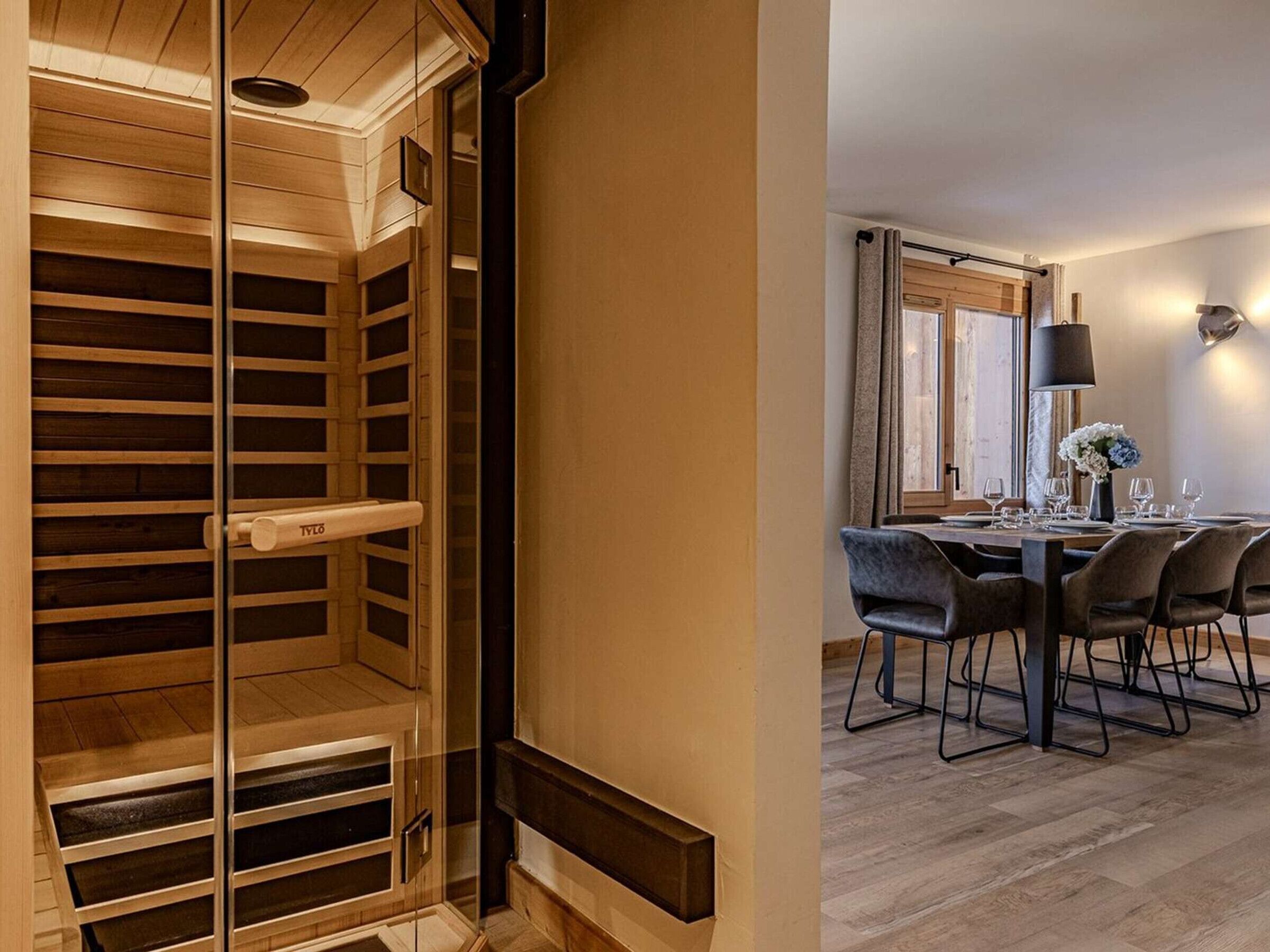 Un interior modern amb una escala de fusta que mena a un altell, una zona de menjador amb taula preparada per a quatre persones i una finestra gran amb cortines.