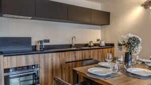 A modern kitchen with wooden cabinetry, a built-in oven, and a dining area with a table set for two. - Chic apartment in Belle Plagne - 6 guests (Belle Plagne)