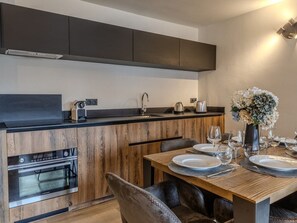 A modern kitchen with wooden cabinetry, a built-in oven, and a dining area with a table set for two. - Chic apartment in Belle Plagne - 6 guests (Belle Plagne)