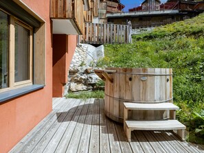 A wooden outdoor deck with a stone wall, a wooden hot tub, and a wooden bench. - Luxury apartment in center - 6 guests (Belle Plagne)