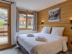 A bedroom with a wooden headboard, a bed with white linens, two bedside lamps, and a window with curtains. - Luxury apartment in center - 6 guests (Belle Plagne)