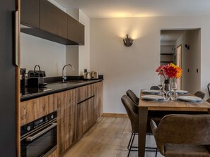 A modern kitchen with wooden cabinetry, a built-in oven, and a dining area with a wooden table set for four. - Luxury apartment in center - 6 guests (Belle Plagne)