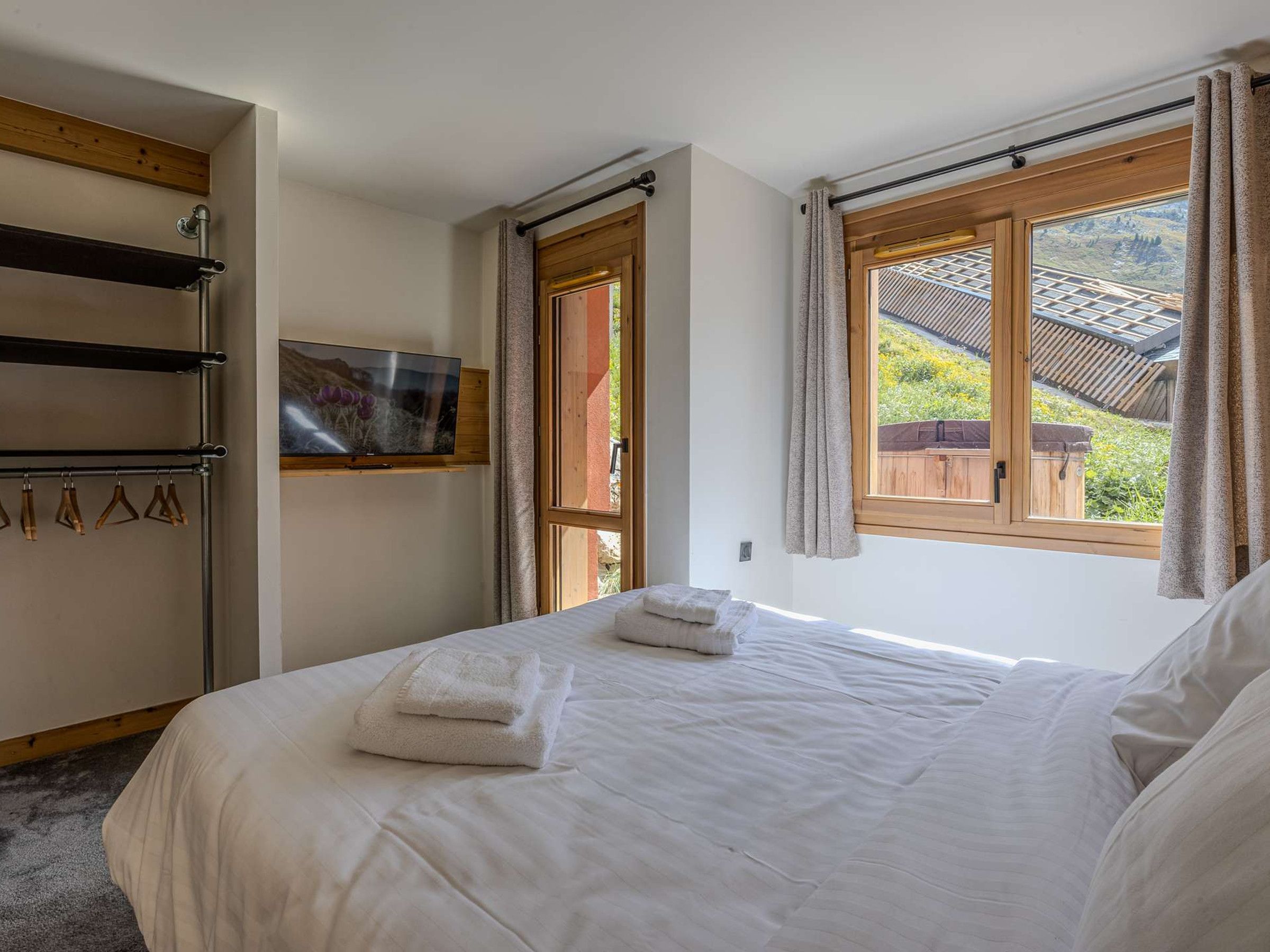 Une chambre à coucher avec un lit, un téléviseur fixé au mur, une fenêtre avec des rideaux et une porte en bois.