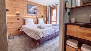A bedroom with a wooden wall, a bed with white bedding, a window, and a bathroom with a wooden cabinet and a mirror. - Luxury apartment in center - 6 guests (Belle Plagne)