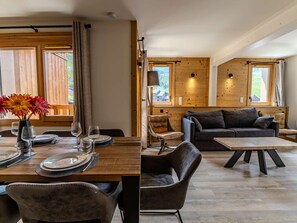 A wooden dining table with chairs, a sofa, and a coffee table in a room with wooden walls and large windows. - Luxury apartment, prime location - 8 guests (Belle Plagne)