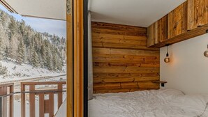 Una camera da letto con una testiera in legno, un letto con biancheria bianca e vista su un paesaggio innevato dal balcone.
