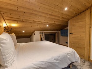 A bedroom with a wooden ceiling, a bed with white bedding, a TV on the wall, and a wooden door. - Cozy mountain duplex - 6 guests (Belle Plagne)