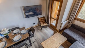 Un coin repas avec une table en bois dressée pour quatre personnes, un canapé, un téléviseur fixé au mur et une porte donnant sur l’extérieur.