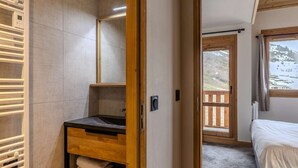 Une chambre avec un lit en bois, une salle de bain avec un lavabo et un espace pour ranger les serviettes, et un balcon offrant une vue sur un paysage montagneux.