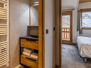 Ein Schlafzimmer mit einem hölzernen Bett, ein Badezimmer mit Waschbecken und Ablage für Handtücher, sowie ein Balkon mit Blick auf eine Berglandschaft.